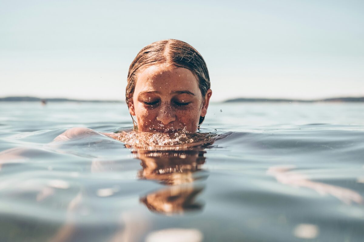 A young person swimming in open water with eyes closed, illustrating water safety for contact lens wearers.