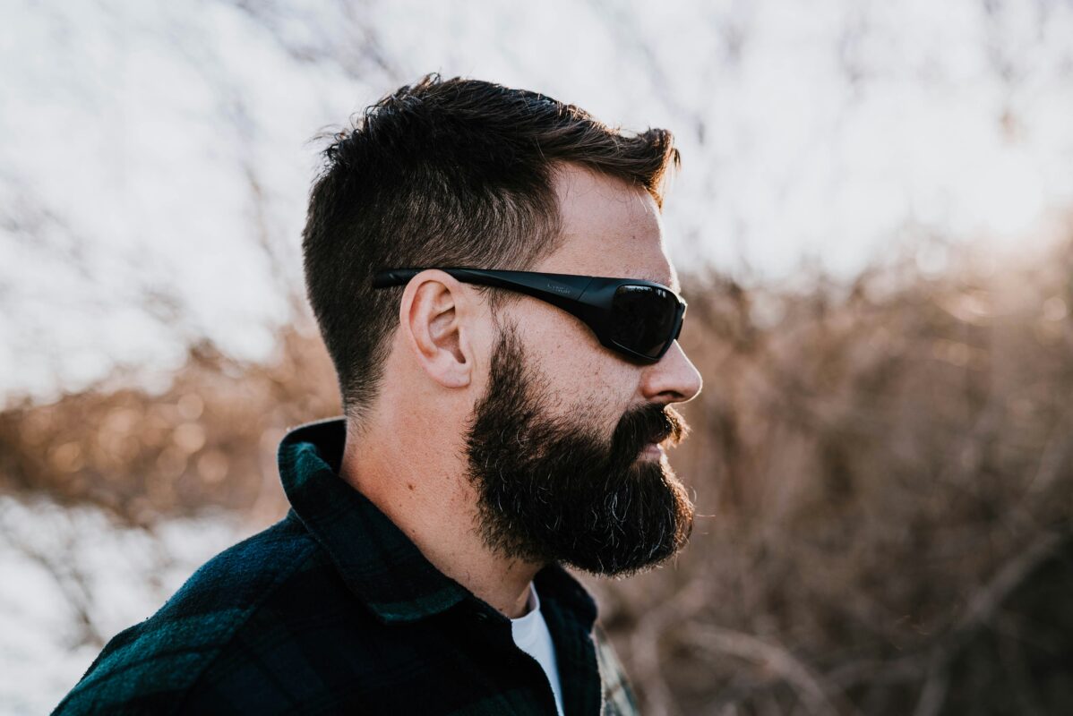 Profile view of a man wearing durable black frame safety glasses outdoors in a workshop environment